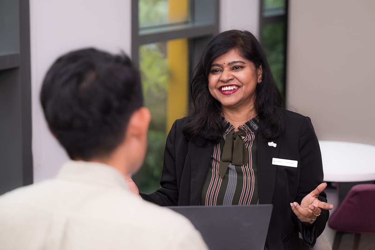 Smiling woman in a blazer gestures while talking to a man, seen from behind.